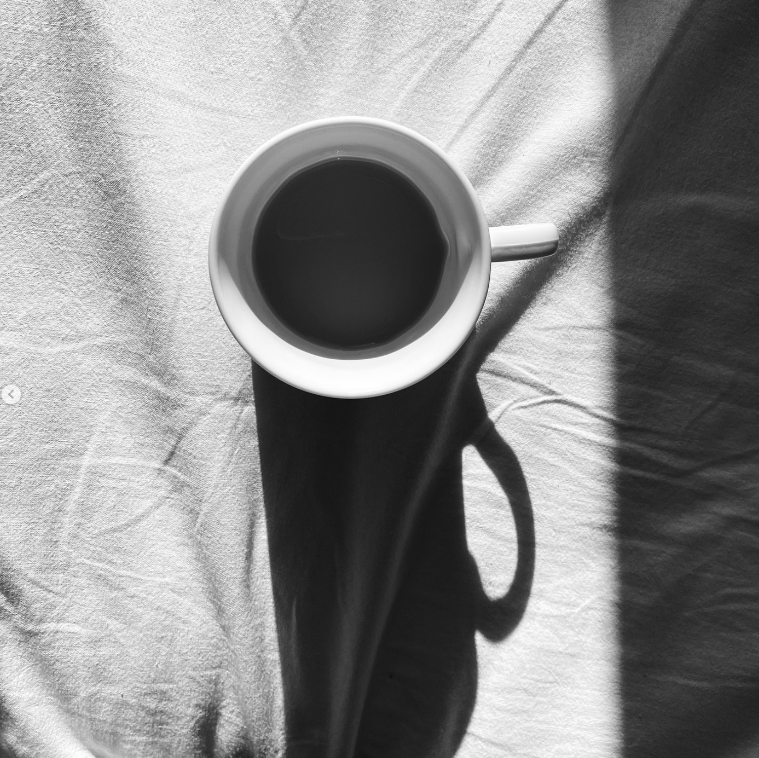 Black-and-white cup of coffee casting a long shadow across rumpled fabric