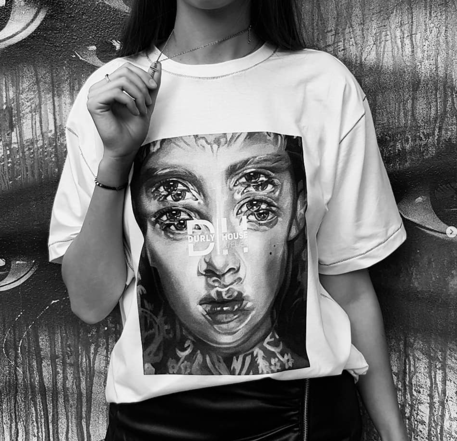 Black-and-white portrait cropped at the face, wearing a graphic T-shirt against a painted mural
