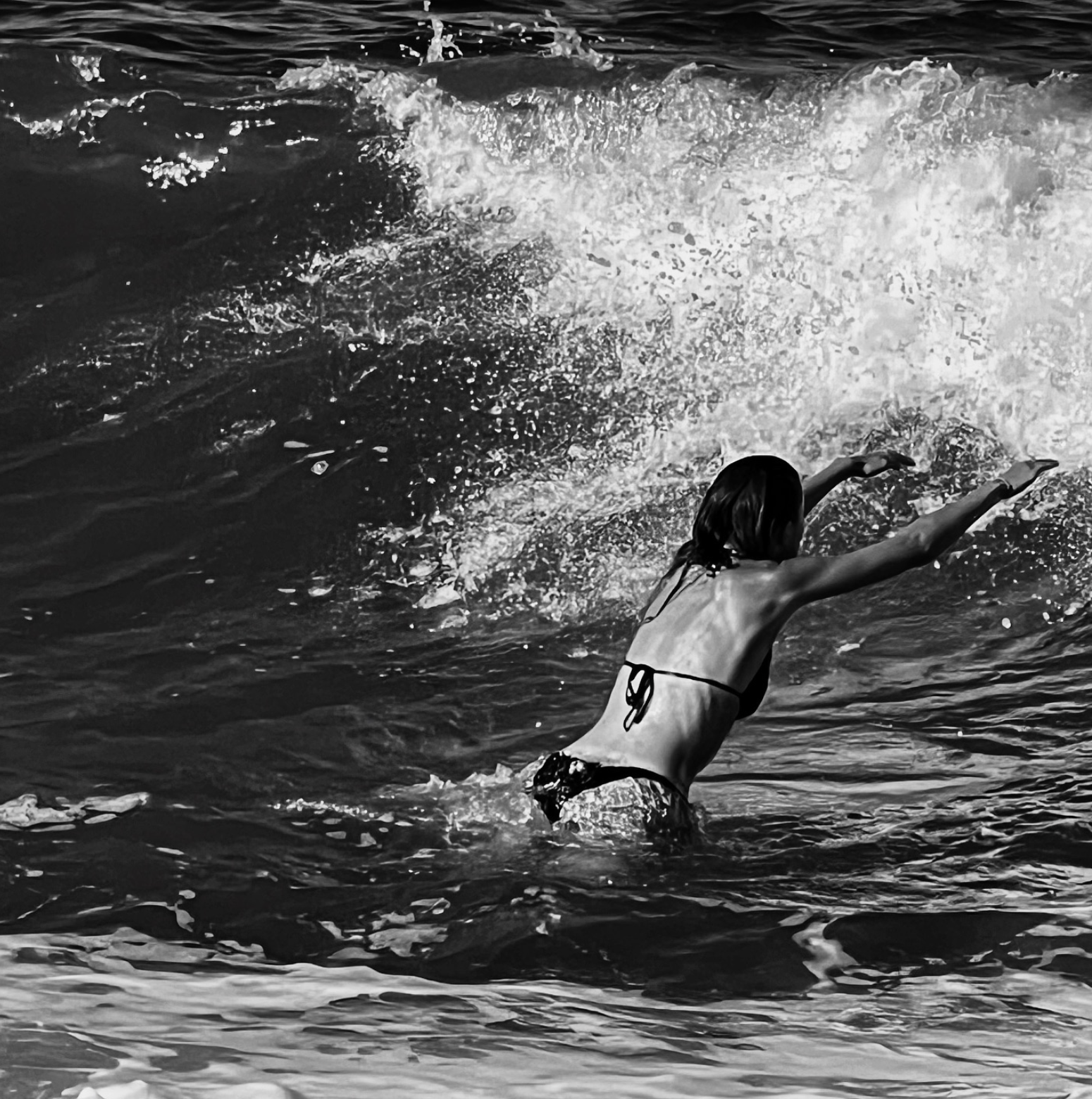 Black-and-white photograph of a woman diving toward a breaking ocean wave