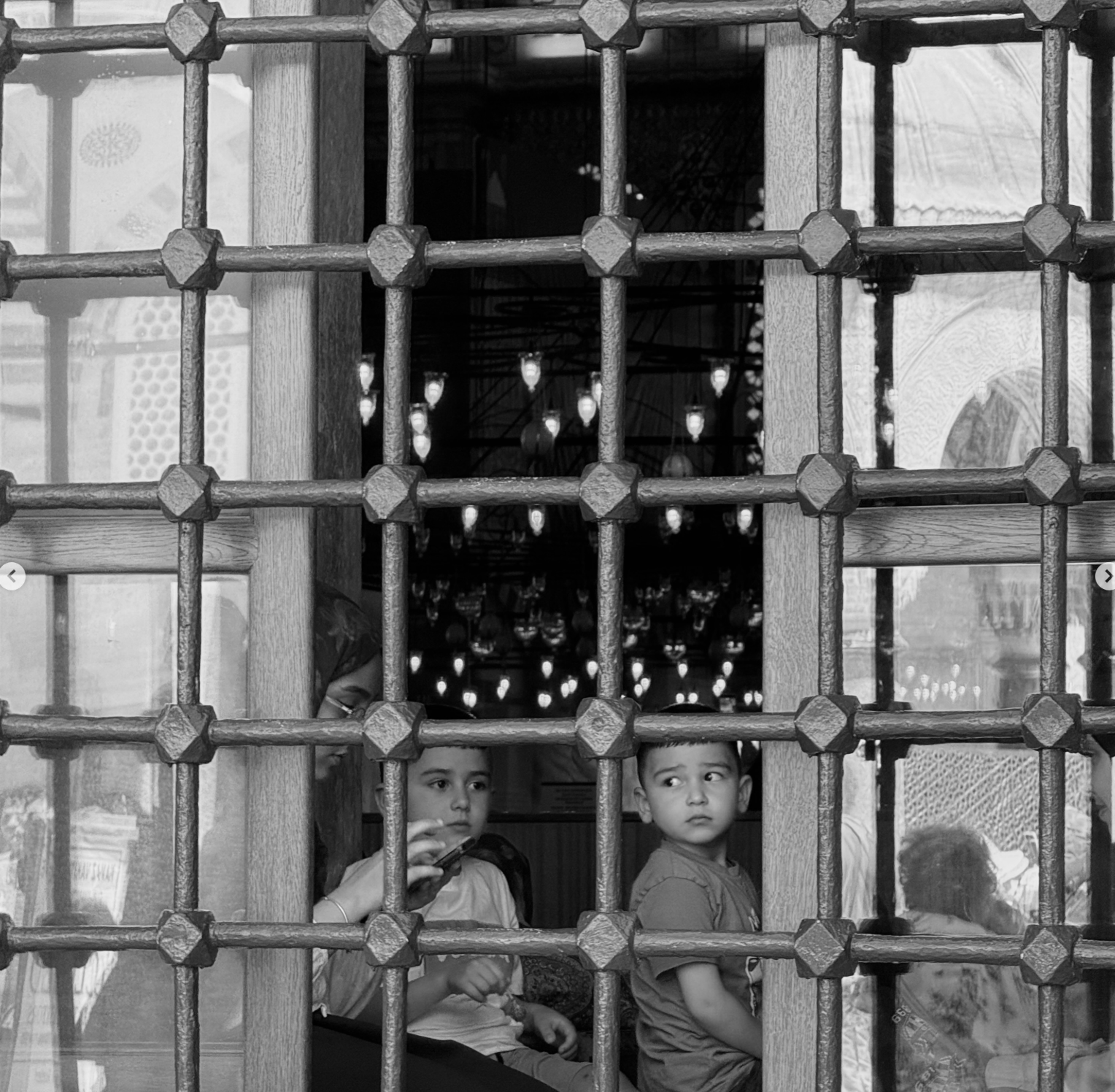Two children looking through a window framed by a geometric iron lattice