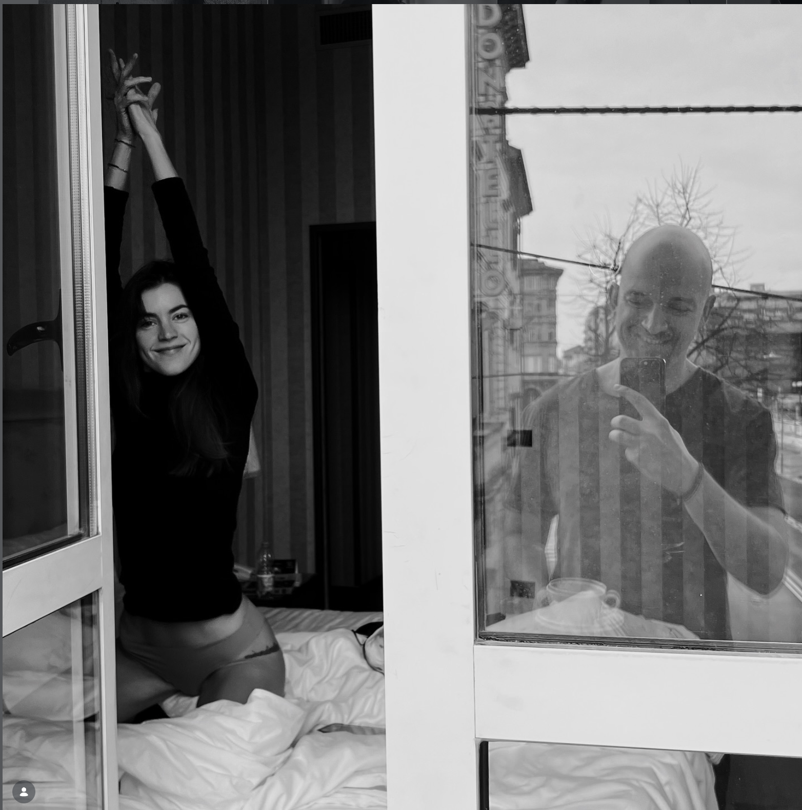Woman stretching inside a room as a man photographs her through the window